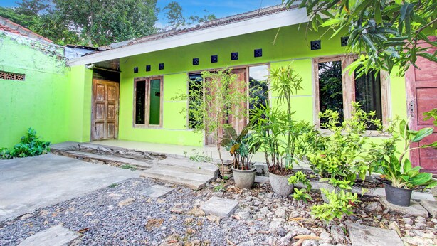 A green building with a tiled roof, wooden doors, and potted plants in the front yard. - Hotel O Juan Kostel 3 (Purwokerto)