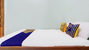 A bed with a white and blue bedspread, two pillows with yellow and blue patterns, and a wooden headboard. - Hotel O Juan Kostel 3 (Purwokerto)