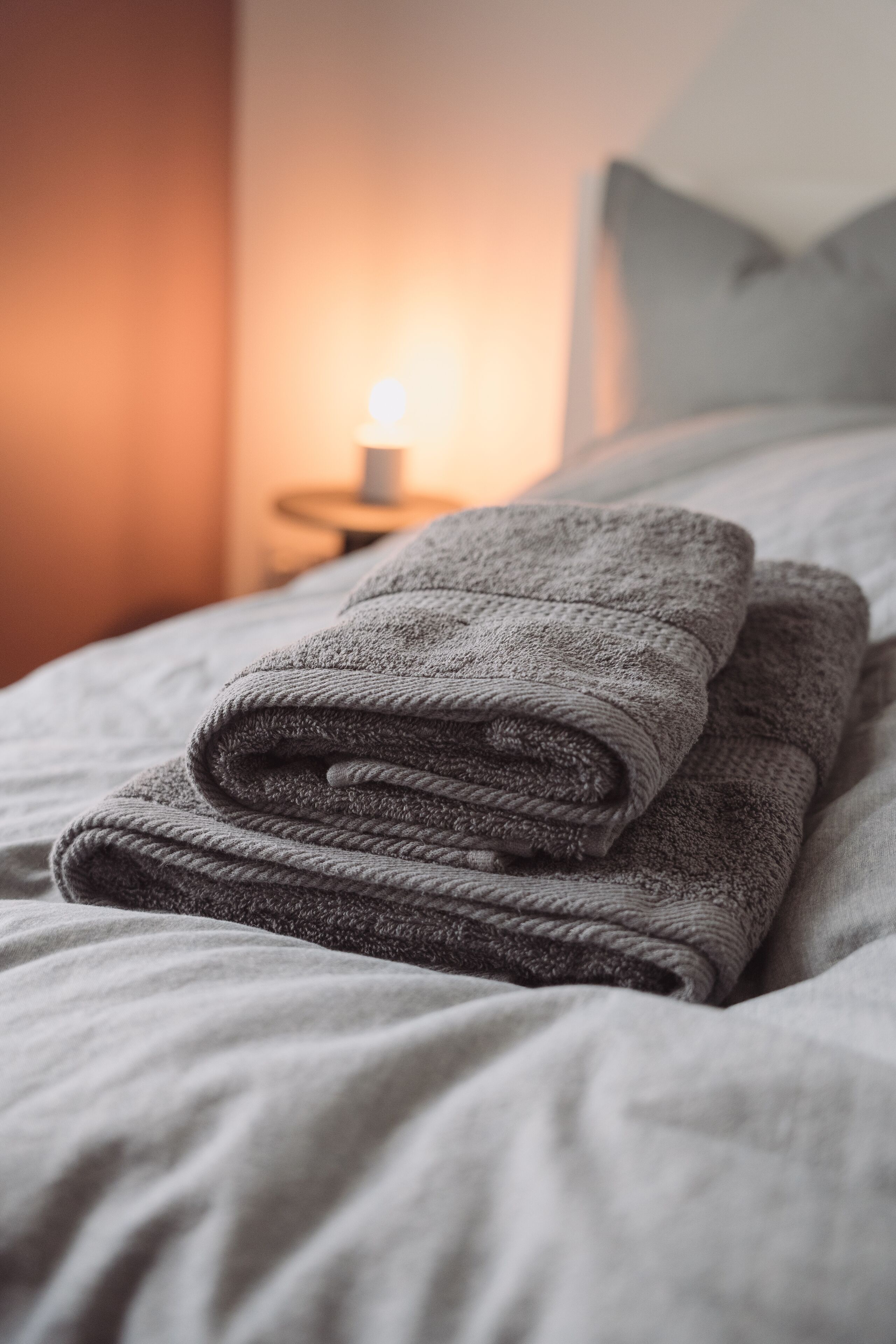 Ein ordentlich gefaltetes graues Handtuch auf einem Bett mit weißer Bettdecke.