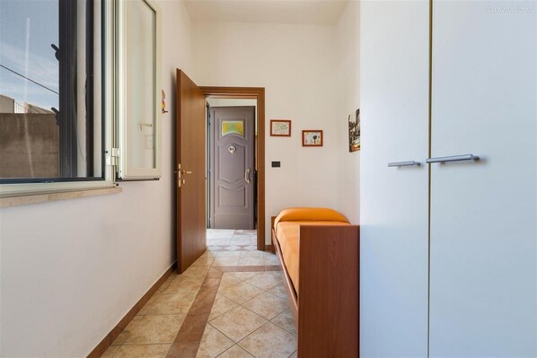 Un pasillo estrecho con una cama, un armario y una puerta que da a otra habitación.