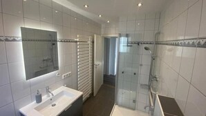 A modern bathroom with a large mirror, a sink, a shower, and a glass-enclosed shower area.