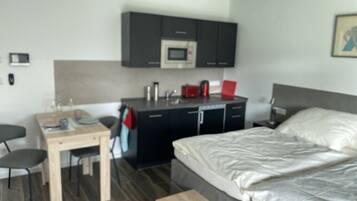 Une chambre d’hôtel moderne équipée d’un lit, d’un bureau, d’une chaise, d’un four à micro-ondes et d’un petit coin cuisine.