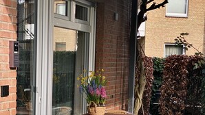 A patio with wicker chairs and a table, a glass door, and a small garden with yellow flowers.