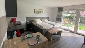 A modern bedroom with a double bed, a small desk, a chair, and a dining table.