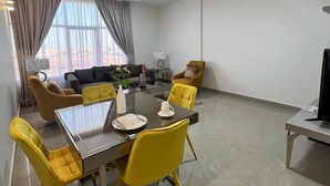 Een moderne woonkamer met een eethoek, met een tafel met glazen blad, gele stoelen, een bank en een televisie.