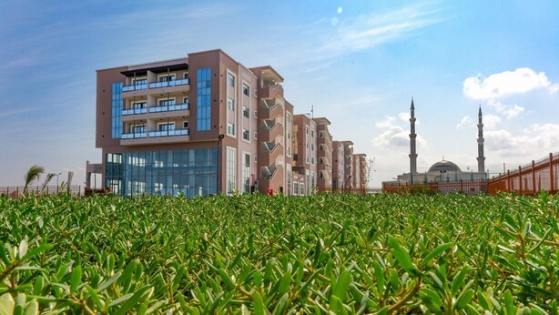 Een modern gebouw met meerdere balkons en een moskee met een minaret op de achtergrond.