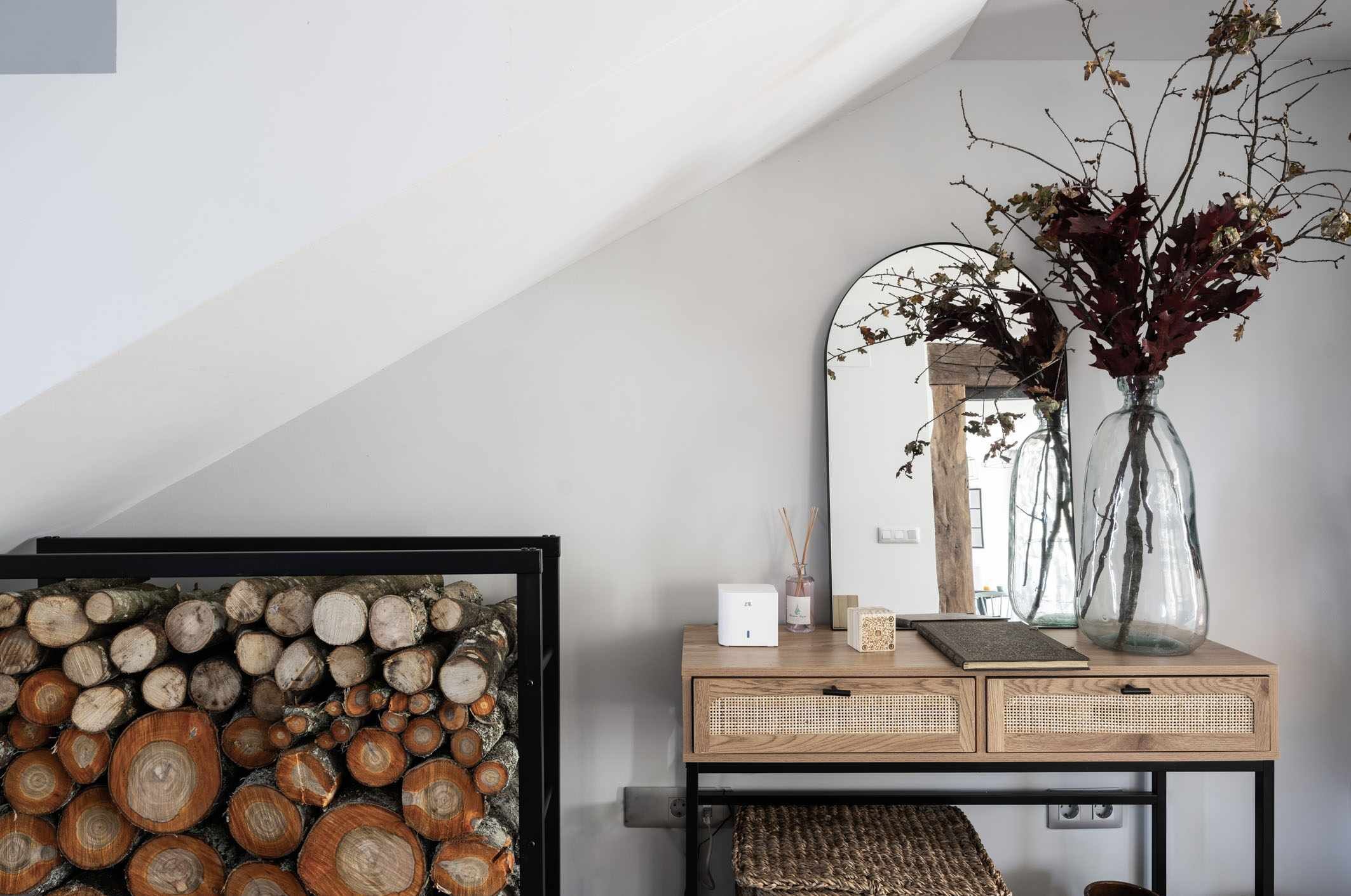 A room with a wooden console table, a mirror, and a vase with branches.