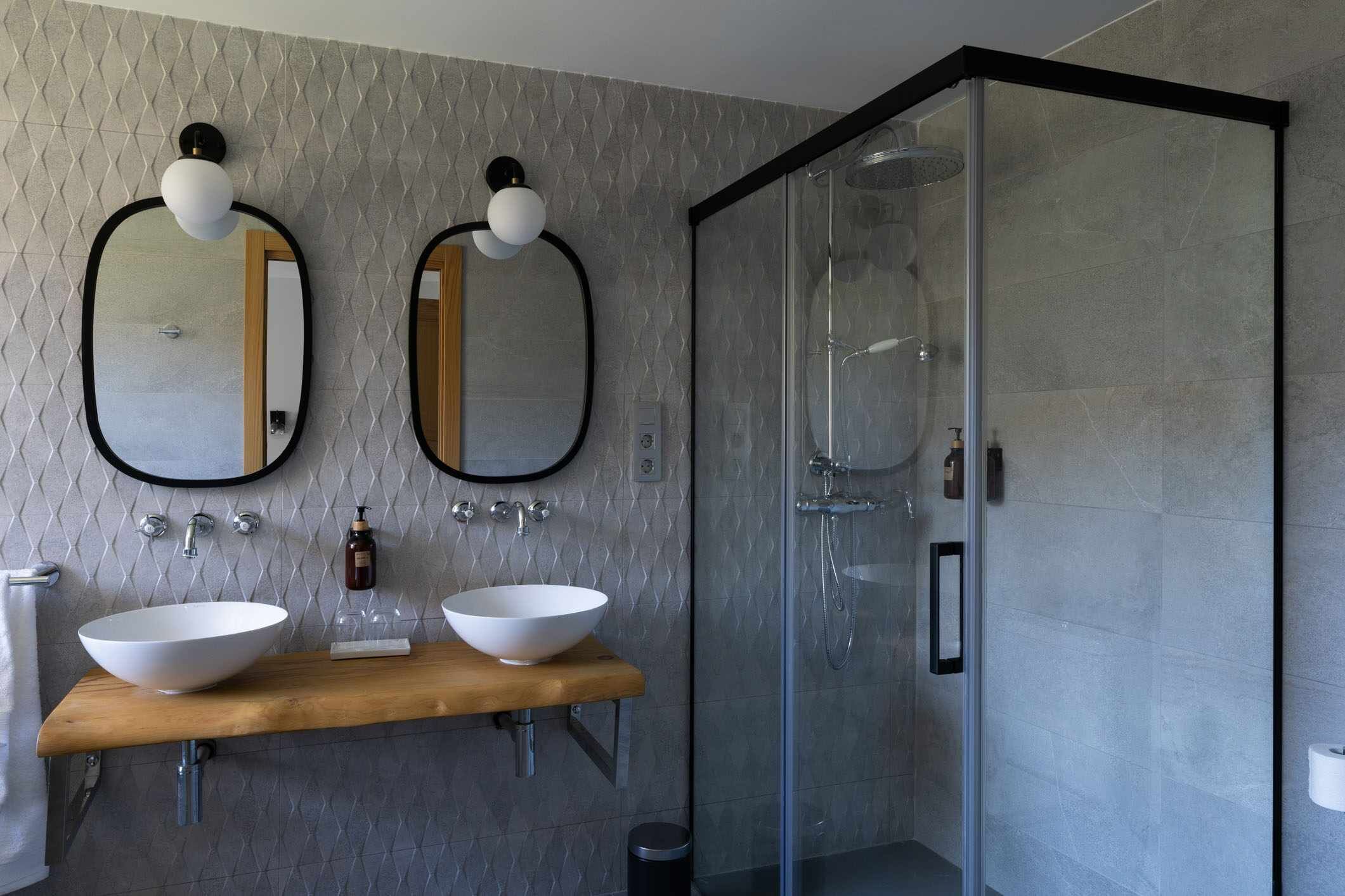 Ein modernes Badezimmer mit zwei Waschbecken, einem großen Spiegel und einer Glasdusche.