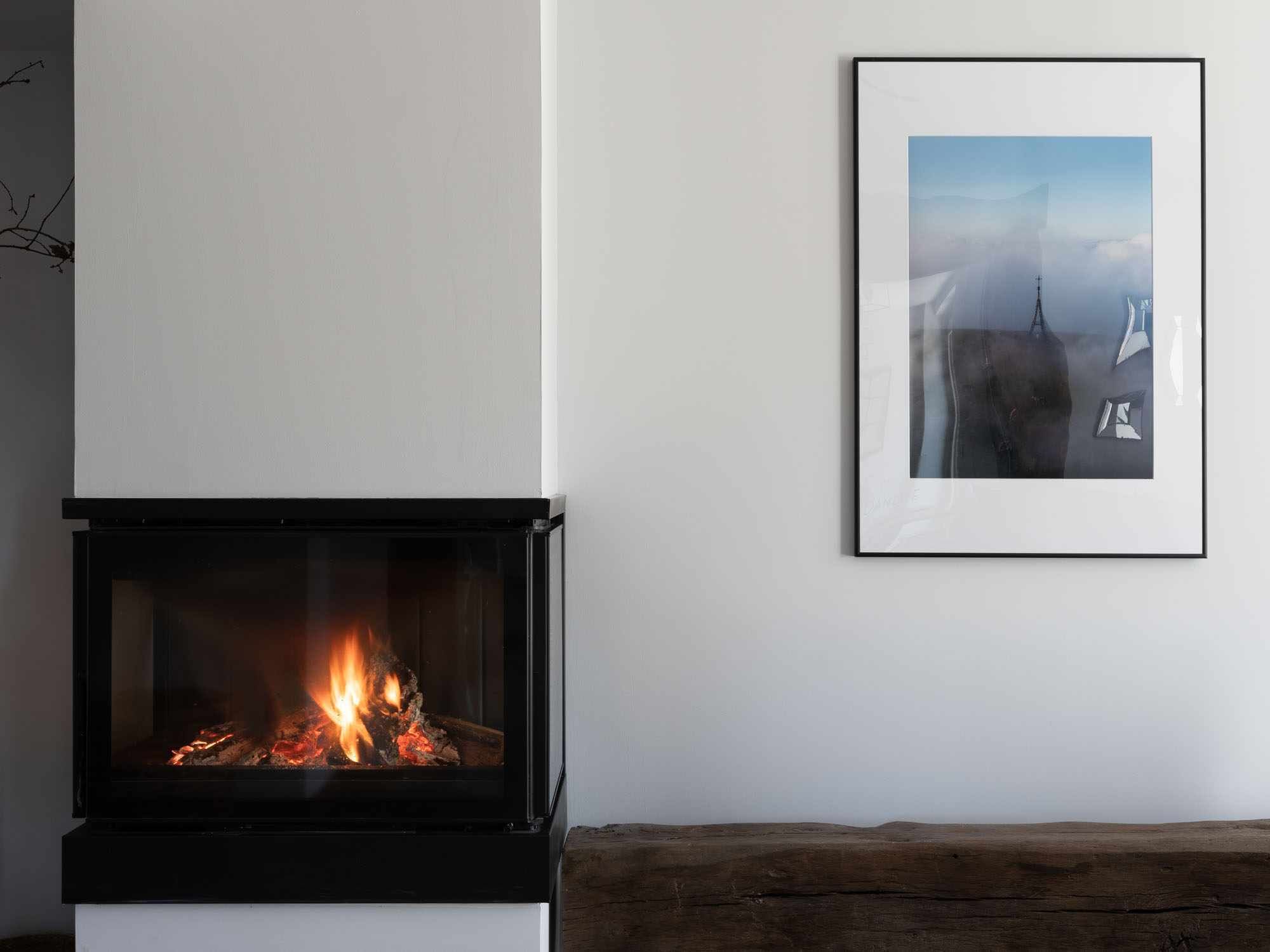 Een moderne haard met een zichtbare vlam, een inlijstbaar beeld aan de muur, en een houten bank.