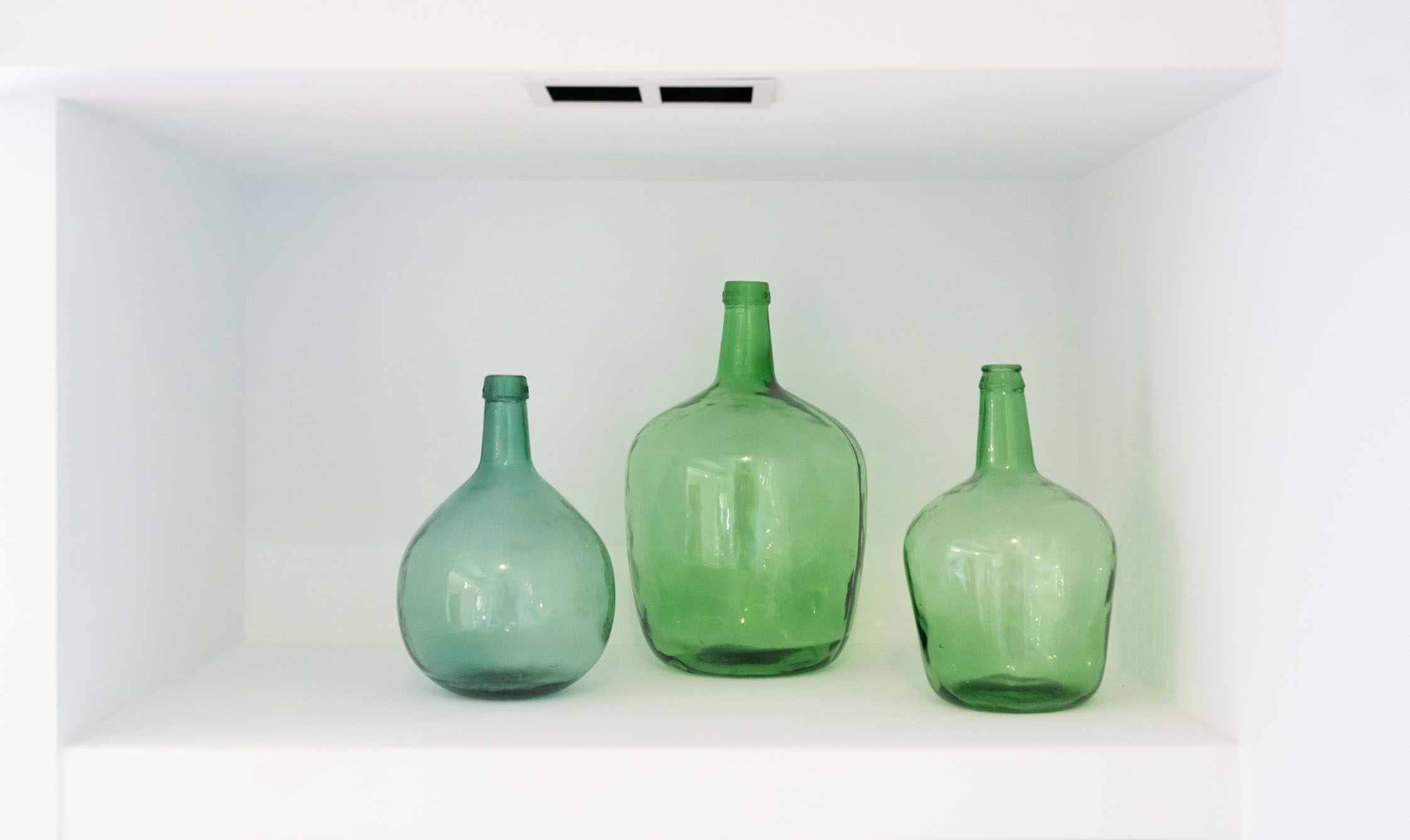 Trois bouteilles en verre vert sur une étagère blanche.