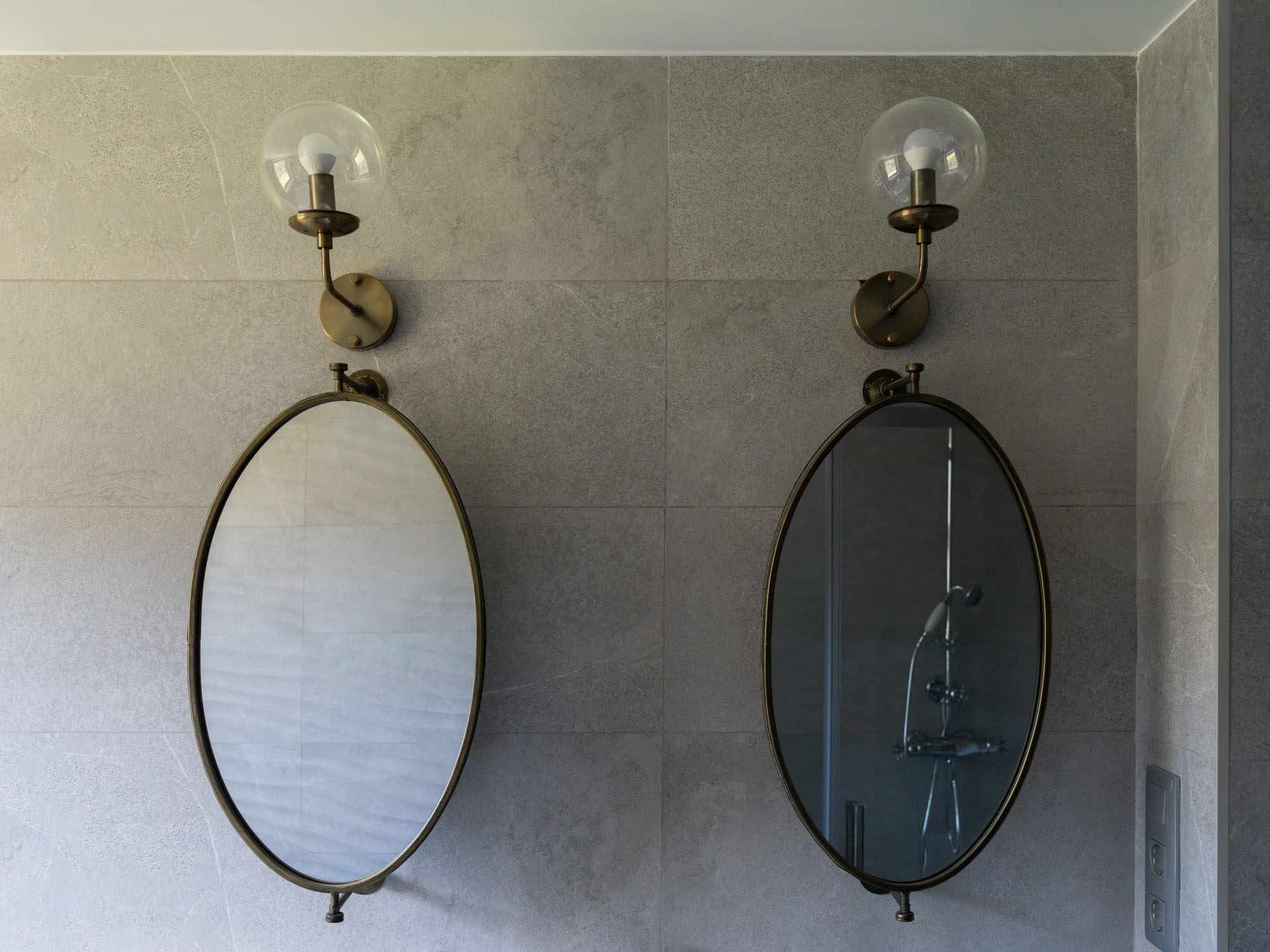 Dos espejos ovalados sujetos a una pared texturizada, cada uno con una bombilla de vidrio transparente arriba.