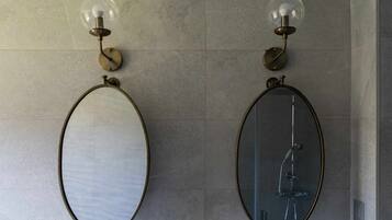 Dos espejos ovalados sujetos a una pared texturizada, cada uno con una bombilla de vidrio transparente arriba.