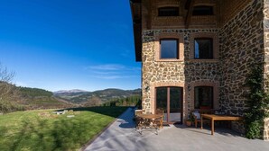 A stone building with a patio, outdoor seating, and a view of mountains. - Izadi (Zeanuri)