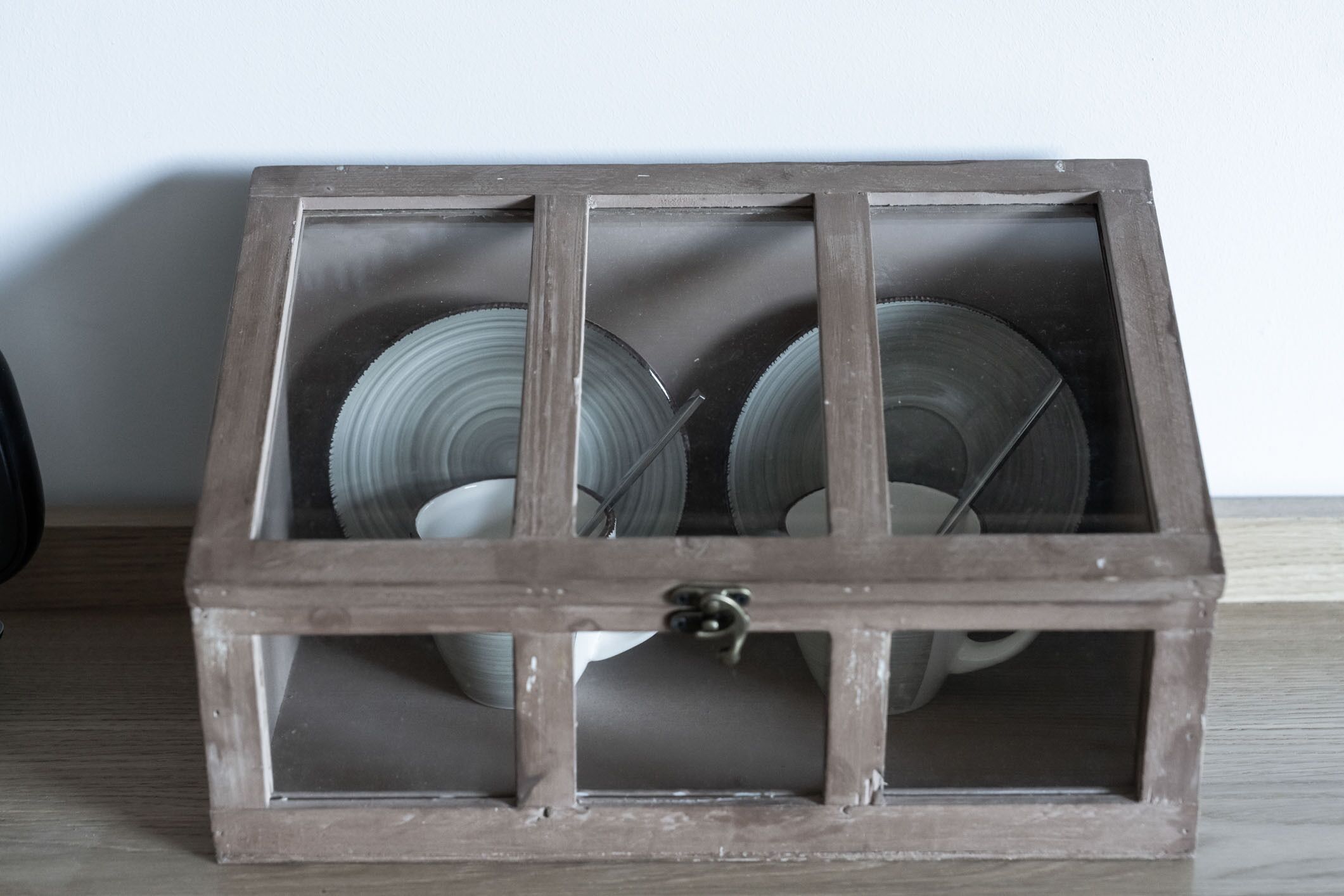 Un meuble rustique en bois, doté d’une porte en verre, contenant plusieurs assiettes en verre et un ustensile en métal.