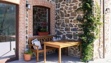 Un muro de piedra con un banco y una mesa de madera, una planta en maceta y una ventana.