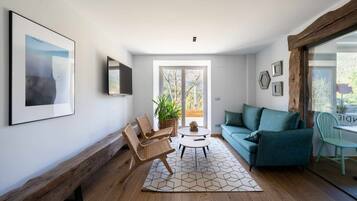 Una sala moderna con un banco de madera, dos sillas de mimbre, un sofá color turquesa, una mesa de centro y un ventanal con vistas a árboles.