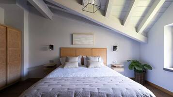Un dormitorio con una cama grande, cabecera de madera, mesitas de noche, una lámpara de pared y una planta en maceta.
