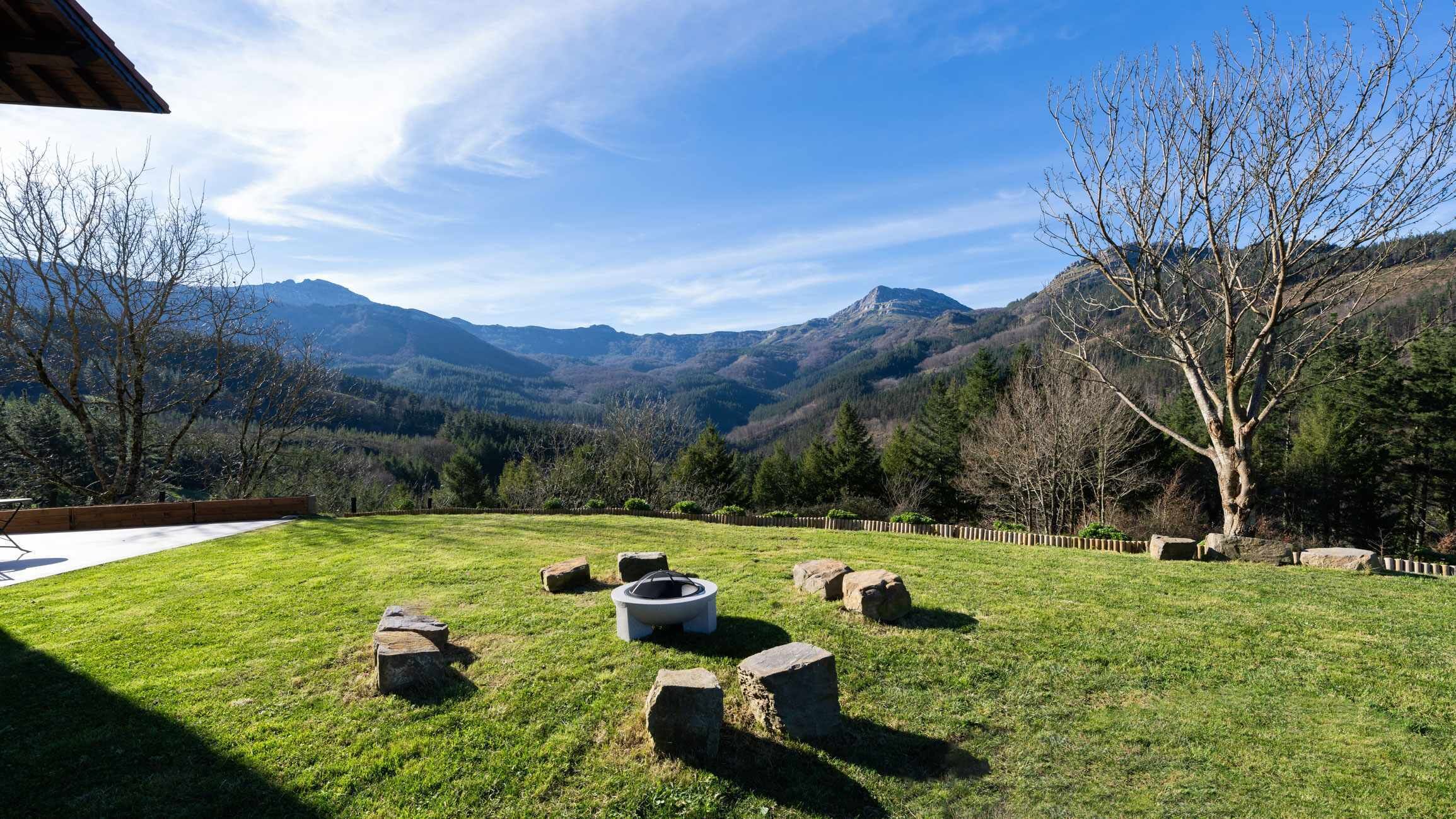 Una zona exterior amb gespa, una xemeneia de pedra, una taula de fusta i una cadira.