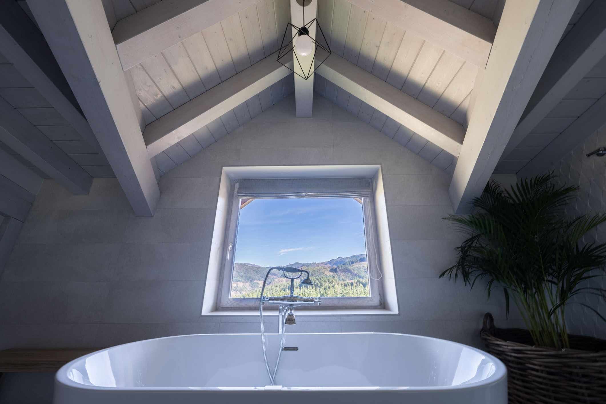 Un baño con una bañera independiente, un ventanal con vistas a montañas y una lámpara en el techo.