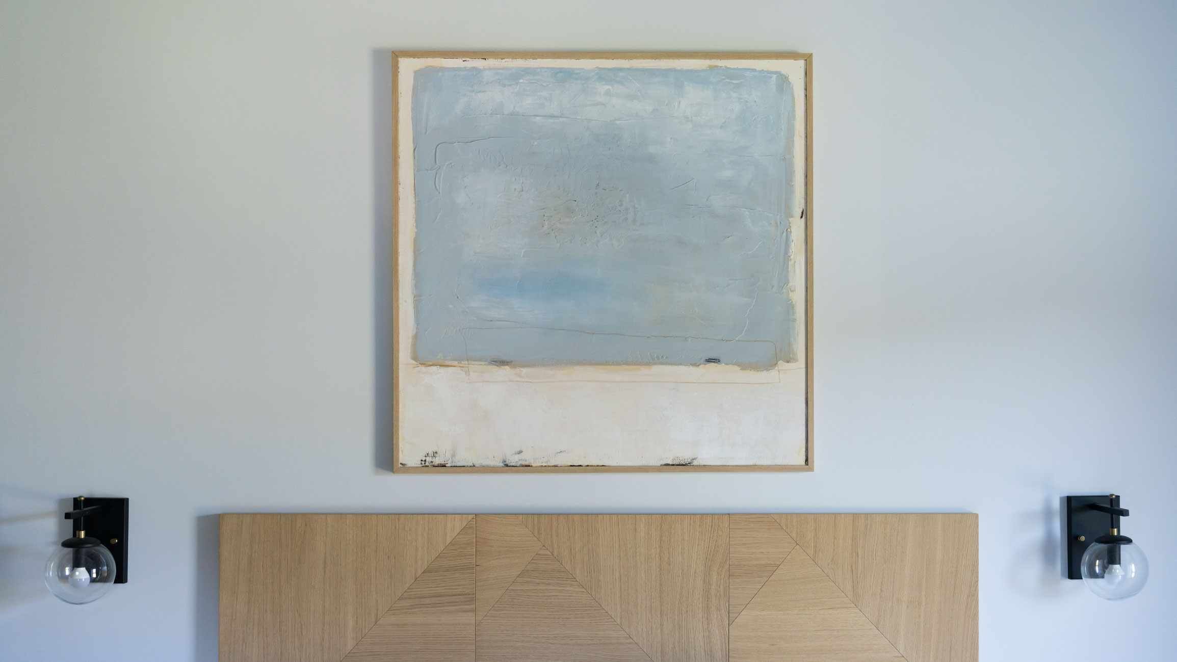 Un baño minimalista con una pared lisa, un cabecero de madera sencillo y dos luces fijadas a la pared.