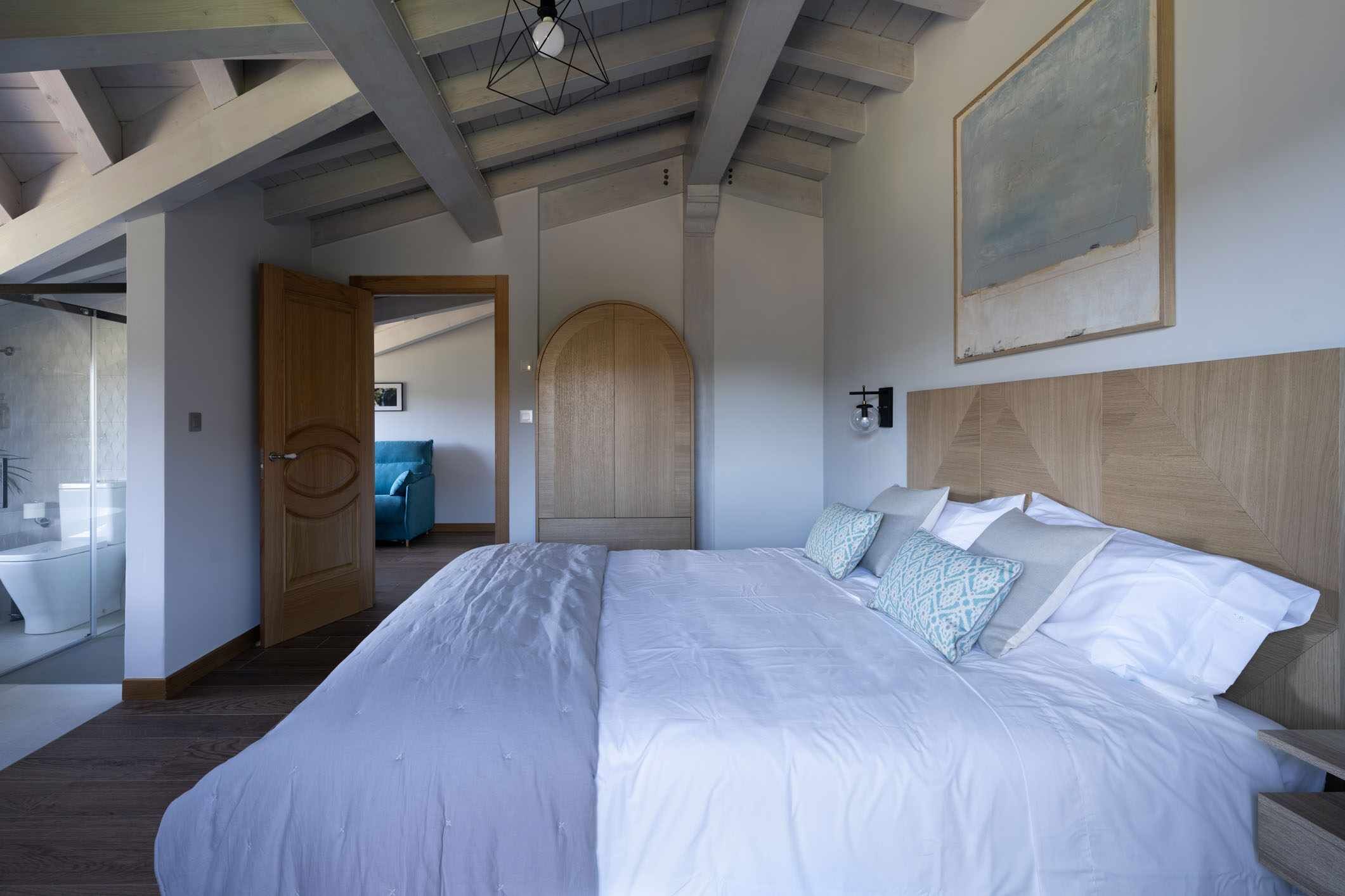 A bedroom with a large bed, wooden headboard, and a view of the bathroom.