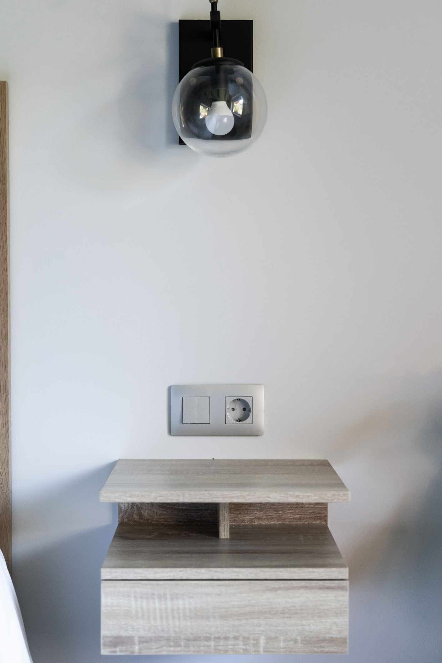 Una lámpara de pared sobre un enchufe y un estante de madera debajo.