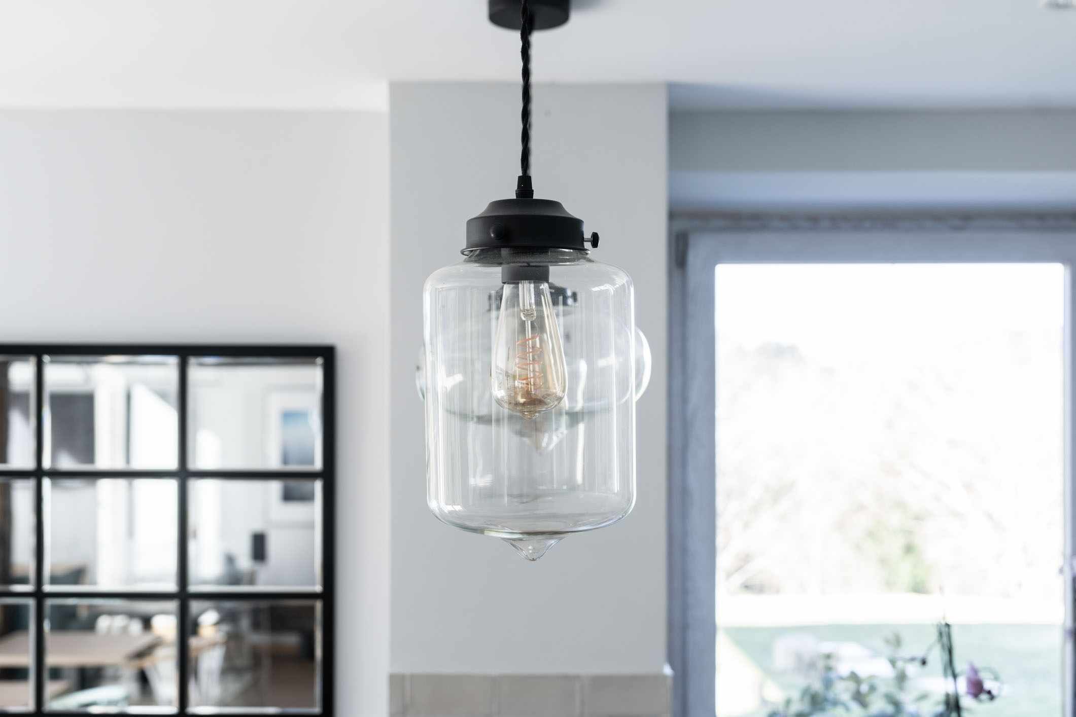 A pendant light with a clear glass enclosure and a visible filament bulb.