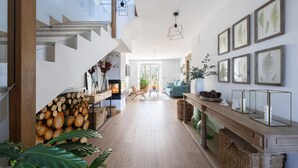 Un interior moderno con una escalera de madera, una sala de estar con sofá y sillones, y una mesa de comedor.