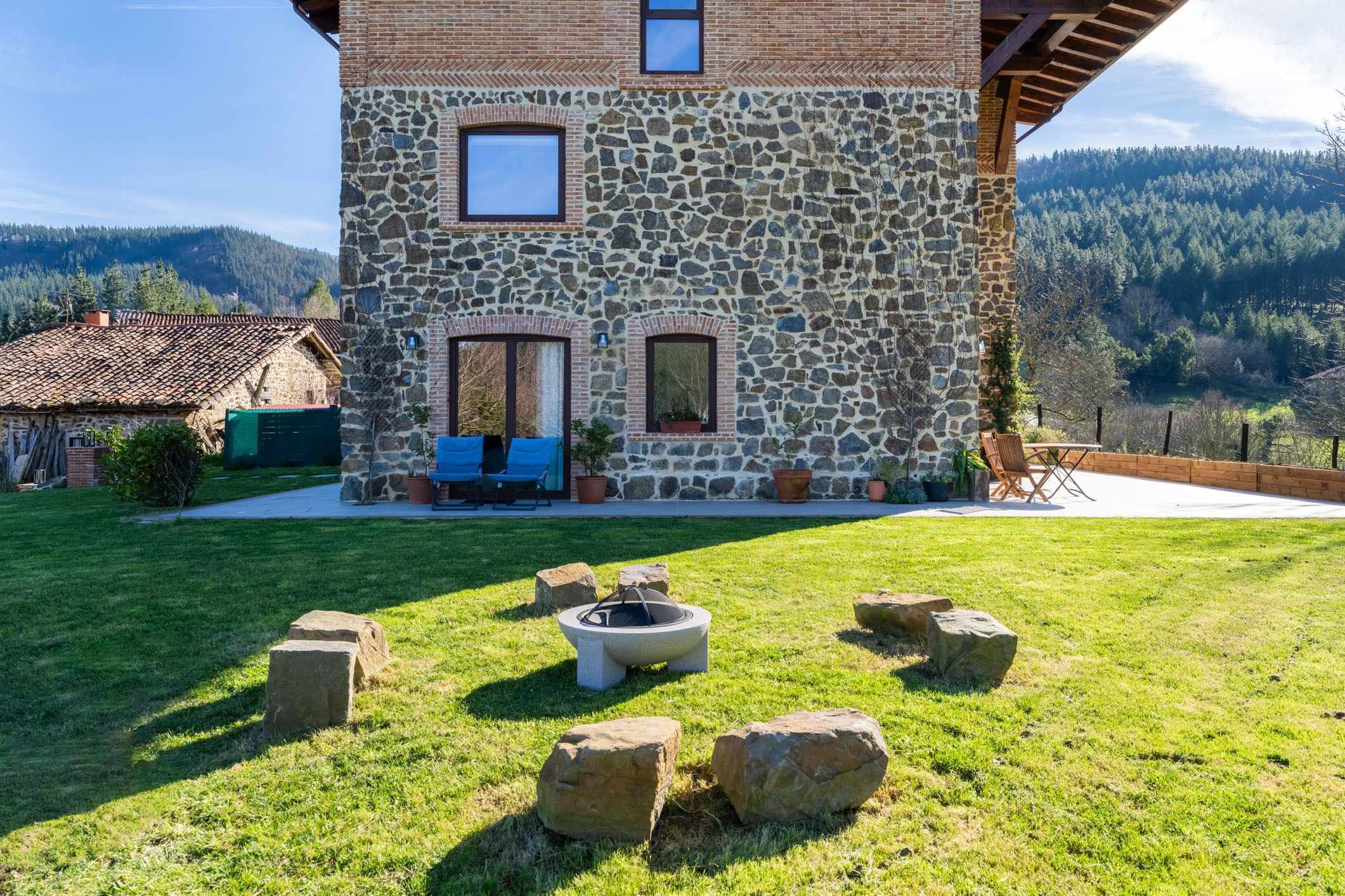 A stone building with a stone fireplace, outdoor seating, and a view of a forested hillside.