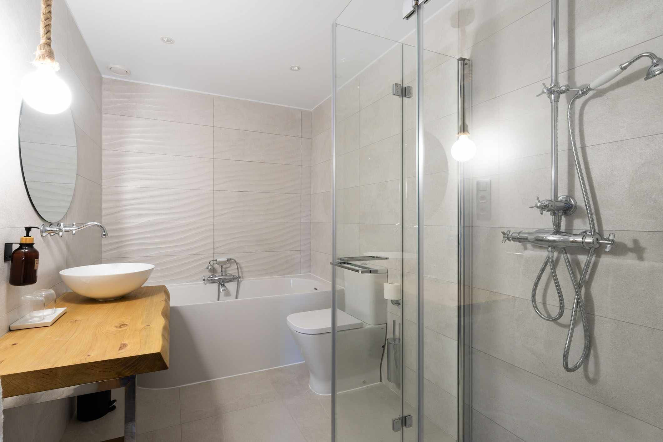 Un baño moderno con ducha envuelta en vidrio, tocador de madera y lavamanos blanco.