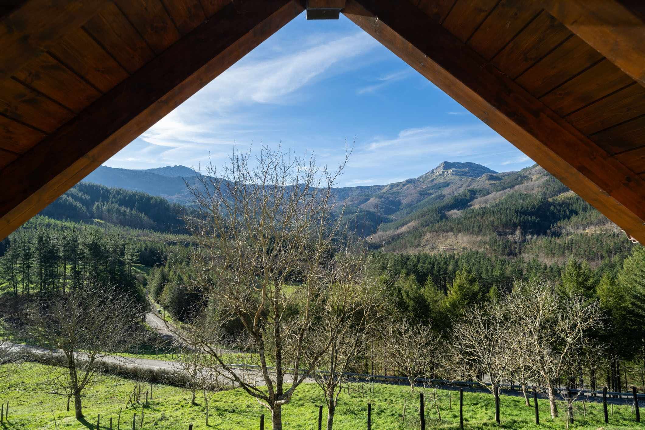 Vista desde una habitación con estructura de madera, mostrando un paisaje montañoso con una carretera y árboles.