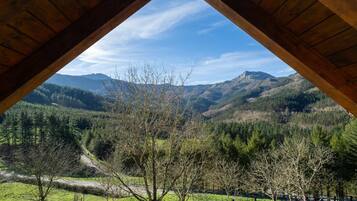 Vista desde una habitación con estructura de madera, mostrando un paisaje montañoso con una carretera y árboles.