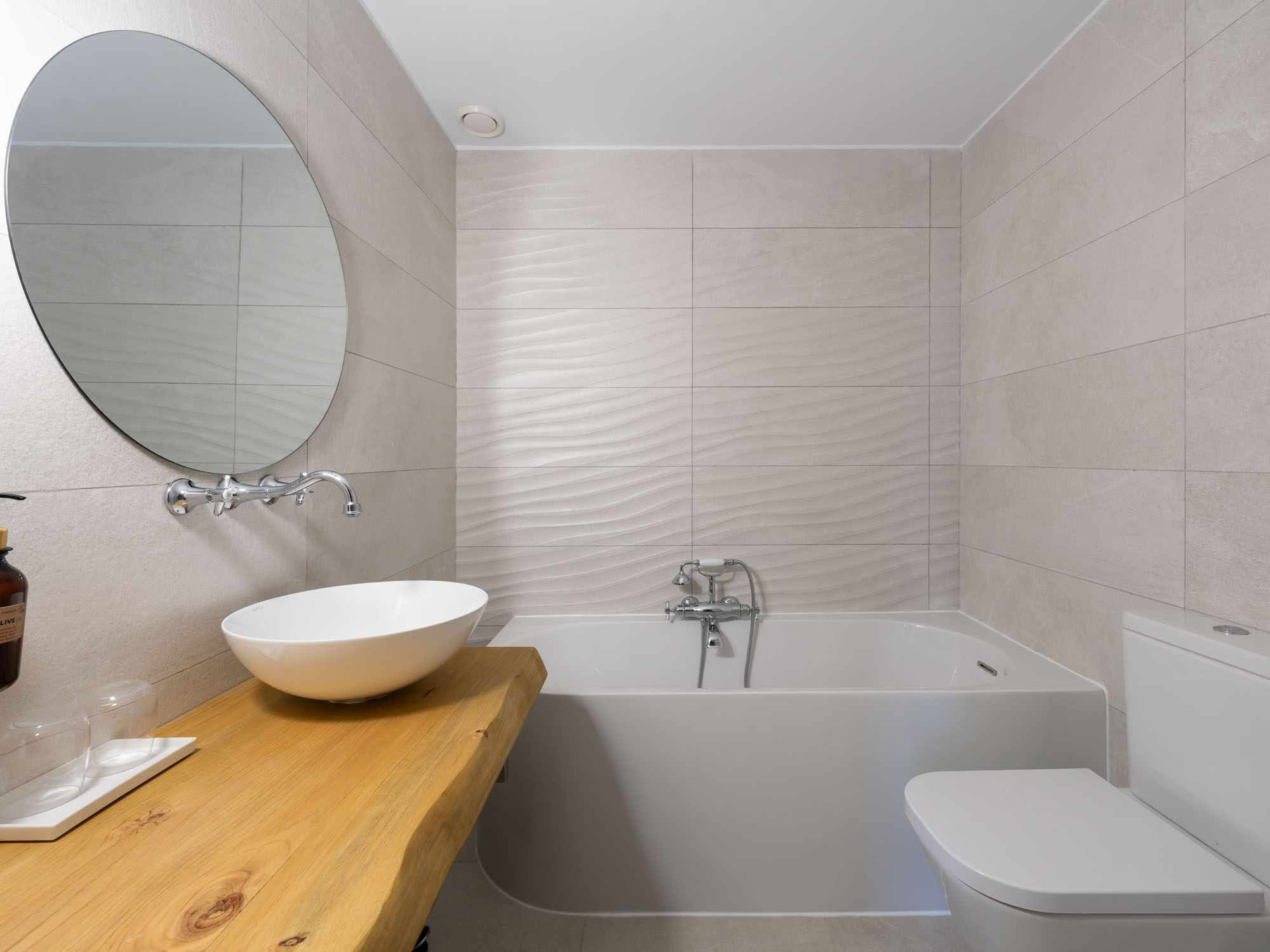 Un baño moderno con una bañera independiente, un espejo redondo y un mueble de tocador de madera.