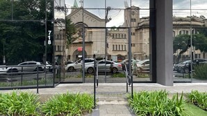 A modern building with a glass facade reflecting a church and parked cars.