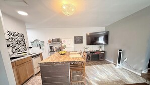 A modern kitchen with a wooden dining table, built-in appliances, and a flat-screen TV mounted on the wall. - Private Entrance Guest Suite Apartment (Burns)