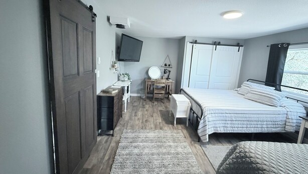 A bedroom with a bed, bedside table, and a TV mounted on the wall. - Private Entrance Guest Suite Apartment (Burns)