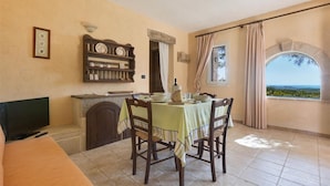 Un coin repas avec une table dressée pour quatre personnes, un téléviseur, une cheminée, une horloge et une fenêtre donnant sur un beau paysage.