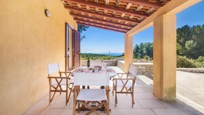 Une terrasse extérieure avec une table dressée pour deux personnes, des chaises en bois et une vue sur le paysage.