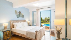 Une chambre avec un lit en bois, une table de chevet avec une lampe, un élément décoratif mural et une vue sur une piscine par une porte ouverte.