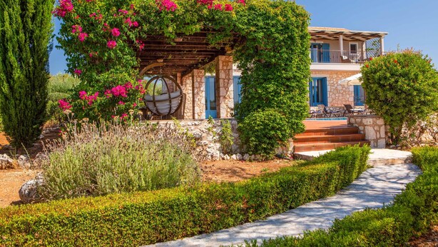 Un bâtiment en pierre avec un jardin, une pergola ornée de fleurs et une piscine.