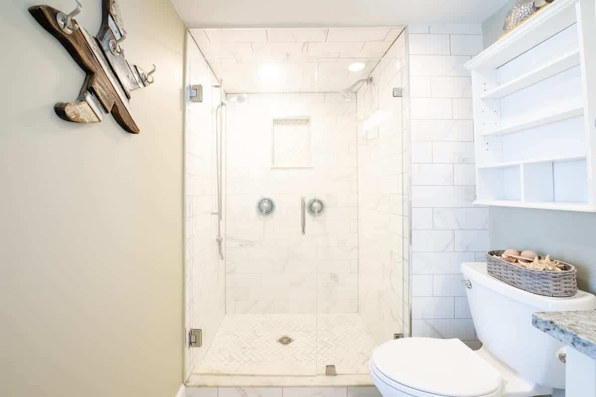 Une salle de bain avec une douche à parois de verre, des toilettes et un mur recouvert de carreaux blancs.