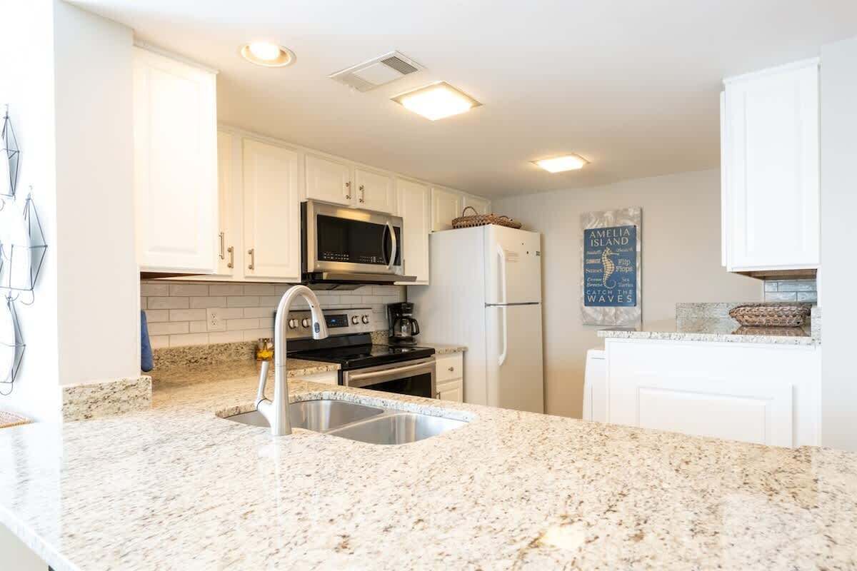 A modern kitchen with white cabinets, a granite countertop, stainless steel appliances, and a backsplash.
