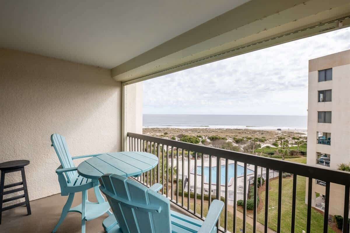 Un balcón con mesa y sillas que da a una piscina y una playa.