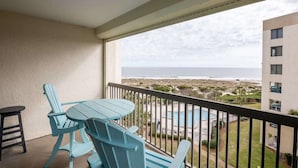 Un balcon avec une table et des chaises, donnant sur une piscine et une plage.