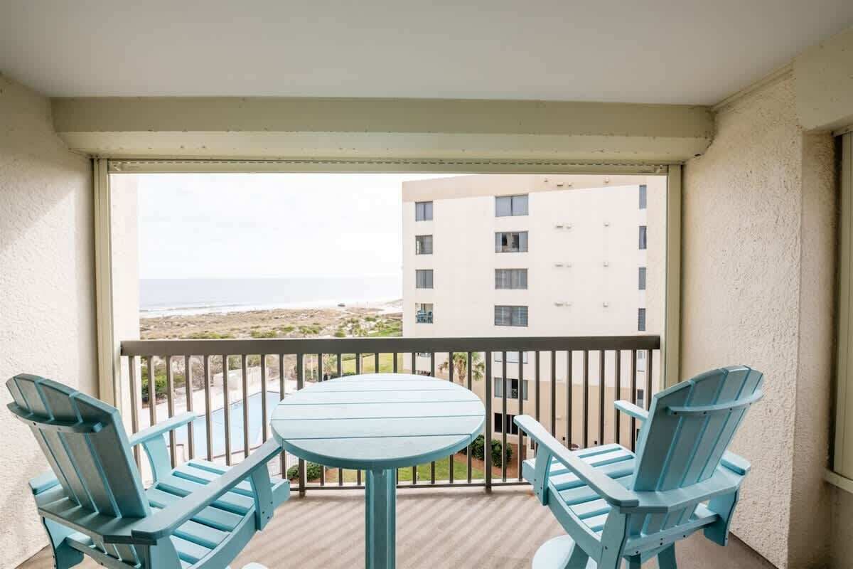 A balcony with a table and four chairs, overlooking a building and a distant view.
