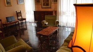 Een kamer met een marmeren vloer, groene fauteuils, een houten tafel en een lamp.