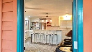 Une cuisine avec des meubles blancs, un îlot central doté de tabourets, et un luminaire suspendu au plafond.