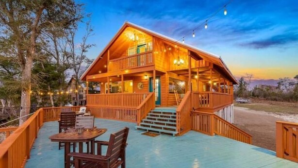 Une cabane en bois à deux étages, dotée d’un balcon et d’un espace extérieur aménagé pour s’asseoir.