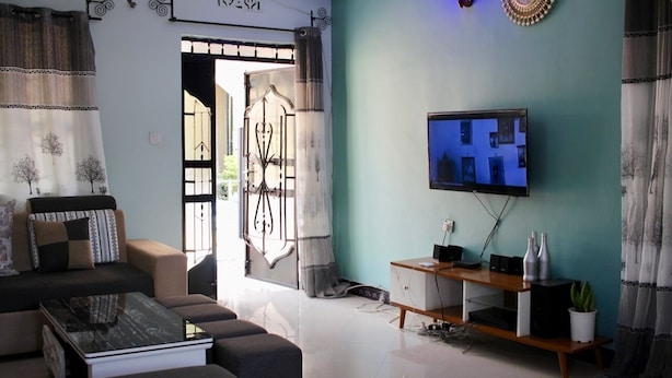 A living room with a sofa, a coffee table, a TV on a stand, and a decorative wall piece. - Bomang'ombe 2 room with breakfast (Boma la Ngombe)