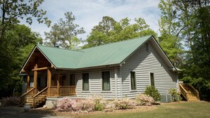 A log cabin with a green roof, wooden porch, and a staircase leading to the entrance. - Family Retreat for vacations, weddings, family reunions and corporate retreats.  (Florence)